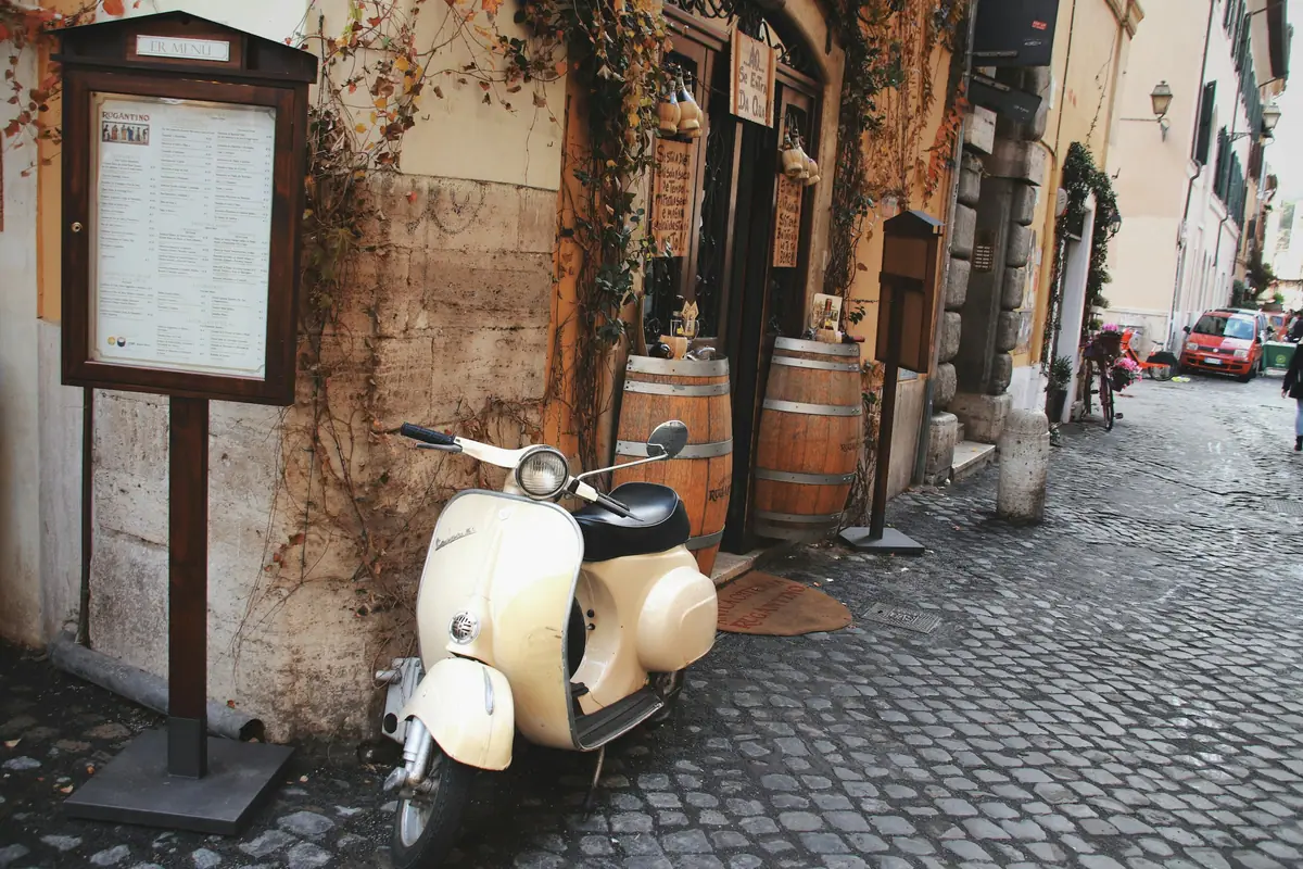 Vespa color crema davanti a una trattoria con botti di legno