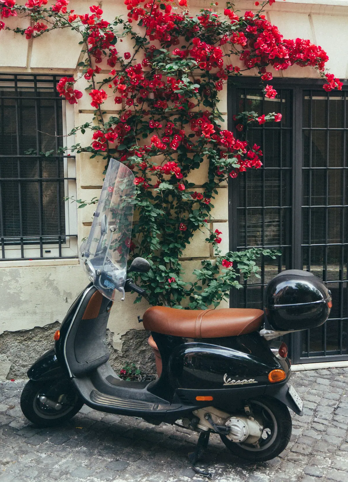 Vespa nera sotto una cascata di bouganville rosse