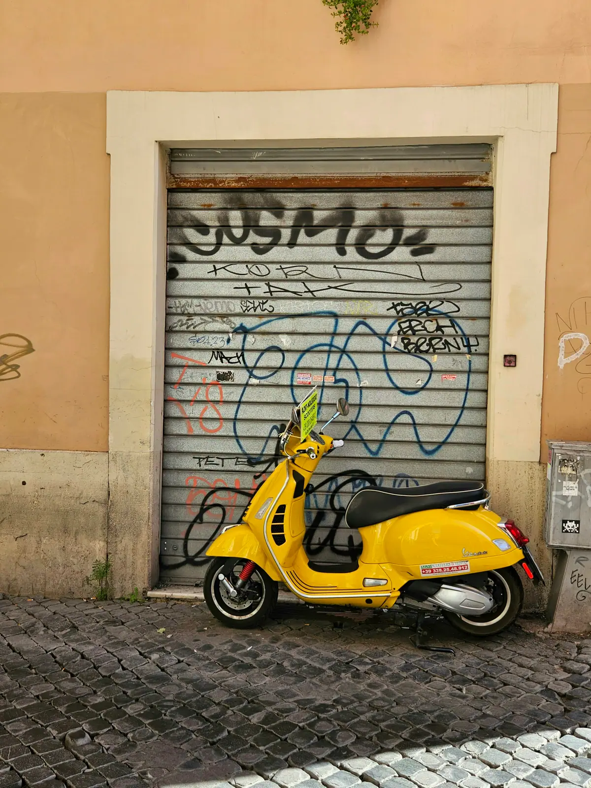 Vespa gialla parcheggiata davanti a una saracinesca in una via romana