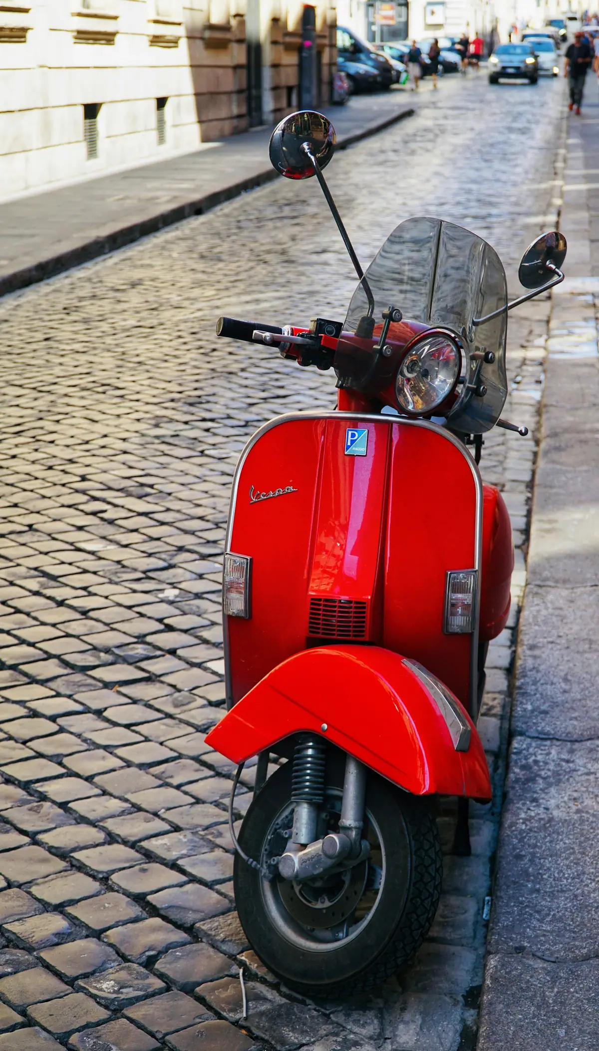 Vespa rossa sul marciapiede di una strada lastricata